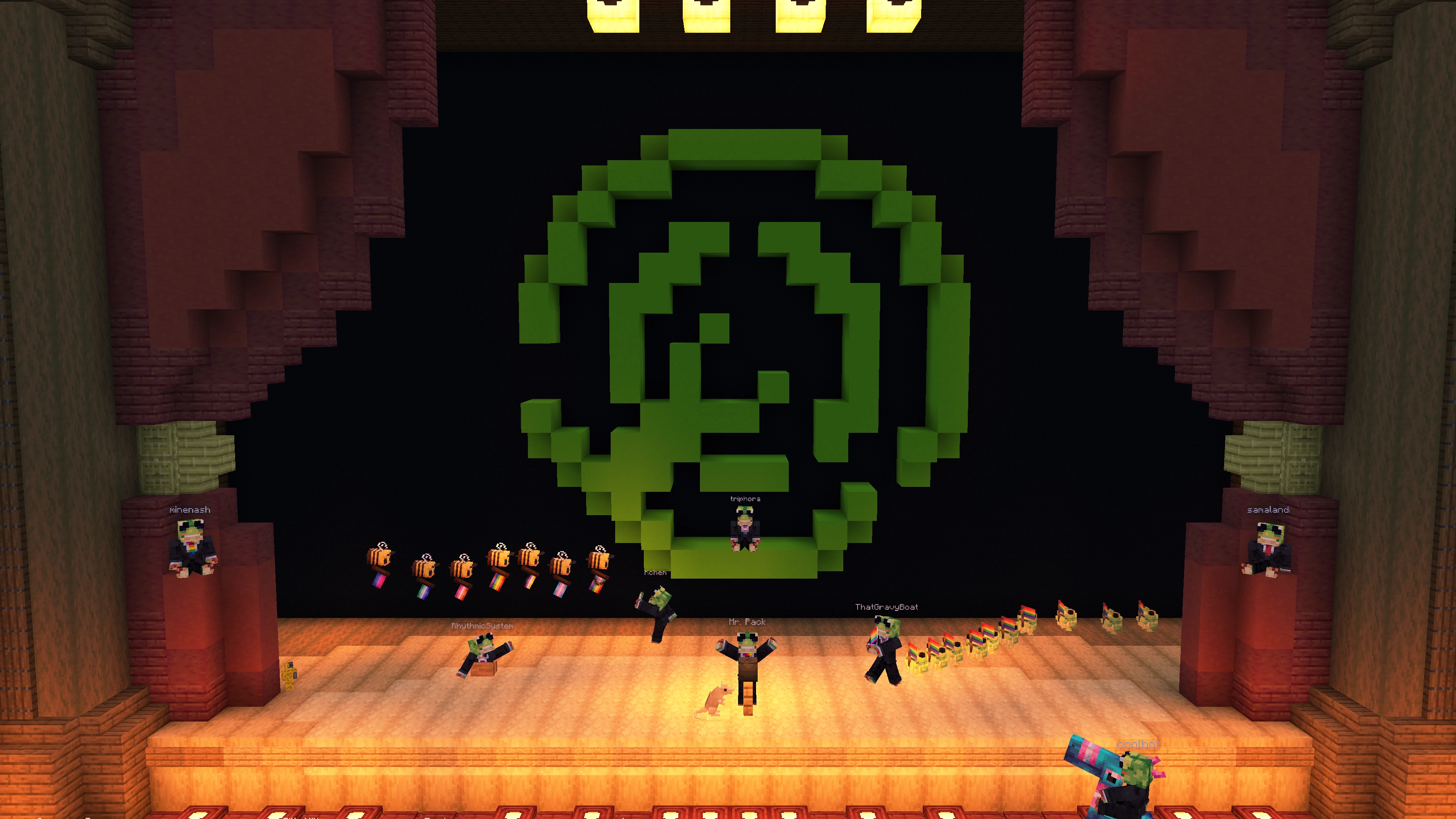 A Minecraft screenshot of a theater stage with a large Modrinth logo, featuring members of the Modrinth team. Mr. Pack is at the very front speaking into a microphone while a staff member leads a Ribbit Pride parade and another leads a bee Pride parade.